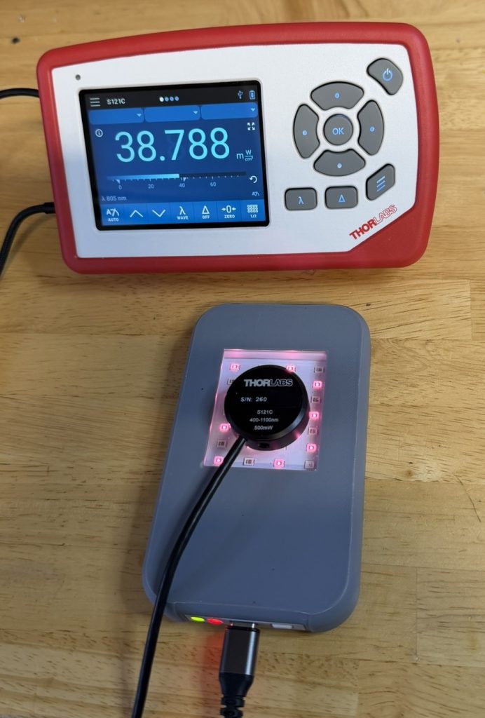 Thorlabs PM100D power meter displaying 38.788 mW/cm² at 805nm NIR wavelength, with S121C sensor in direct contact with a red light therapy device LED array.